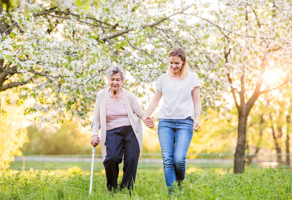 Elderly grandmother with crutch and granddaughter in spring nature.