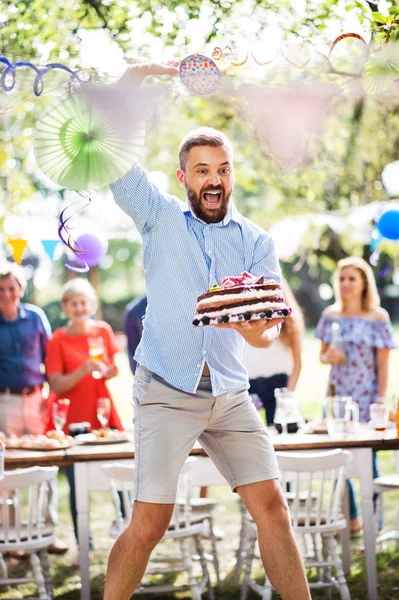Hombre saltando con un pastel en una celebración familiar o una fiesta en el jardín afuera . —  Fotos de Stock