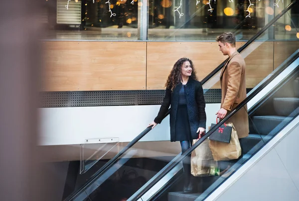 Um jovem casal em uma escada rolante no centro comercial no Natal . — Fotografia de Stock