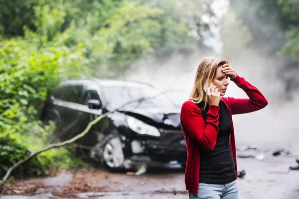 Una mujer joven con teléfono inteligente por el coche dañado después de un accidente de coche, haciendo una llamada telefónica . — Foto de Stock