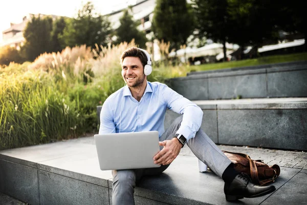 Een zakenman met koptelefoon zitten buiten op trappen, luisteren naar muziek. — Stockfoto