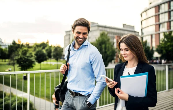 Een jonge zakenman en zakenvrouw lopen op een brug, met behulp van smartphone. — Stockfoto