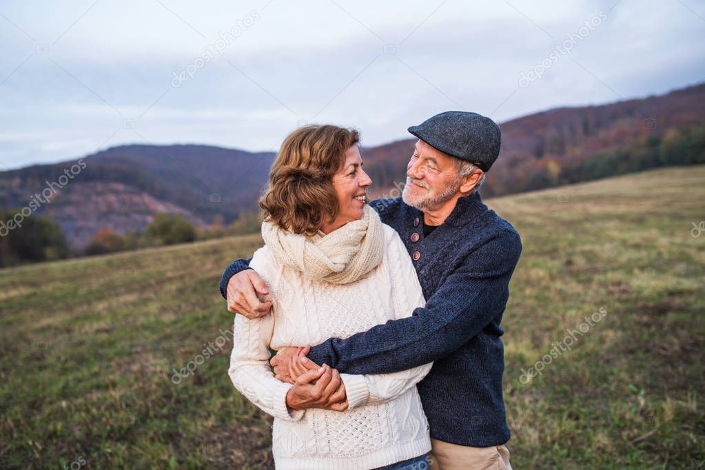 Senior couple in love on a walk in an autumn nature. Senior man and a woman hugging, looking at each other. Copy space.