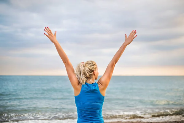 Rear view of young sporty woman runner in blue sportswear standing on the beach. — Stock Photo, Image