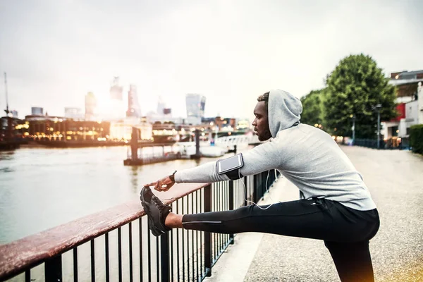 黑色男子赛跑者与智能手机在一个城市的桥梁臂章, 伸展. — 图库照片