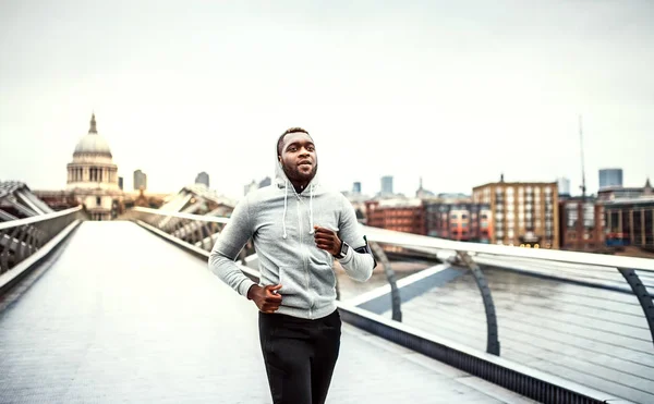 Sportig svart ung löpare kör på bron utanför i en stad. — Stockfoto