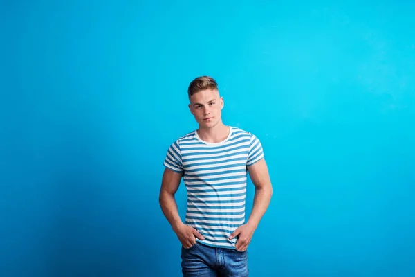 Porträtt av en ung man i en studio stående mot blå bakgrund. — Stockfoto