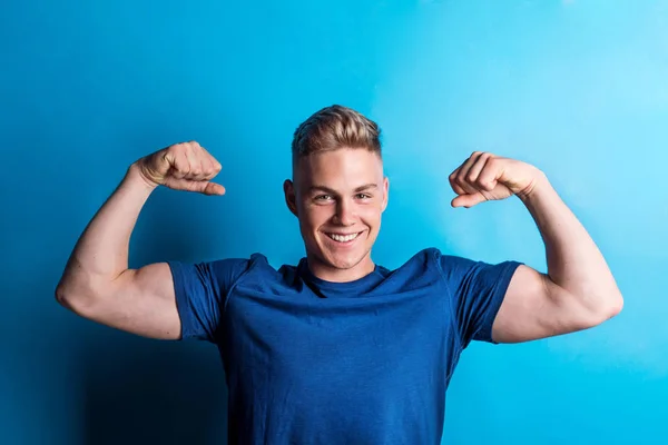 Portrait of a cheerful young man in a studio, flexing muscles. — Stock Photo, Image