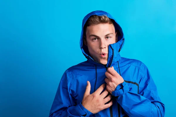 Portrait of a young man with blue anorak in a studio, feeling cold. Copy space. — Stock Photo, Image