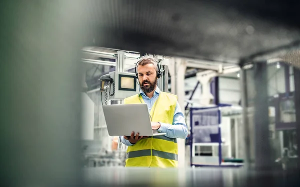 Um engenheiro industrial com fone de ouvido e laptop em uma fábrica, trabalhando . — Fotografia de Stock