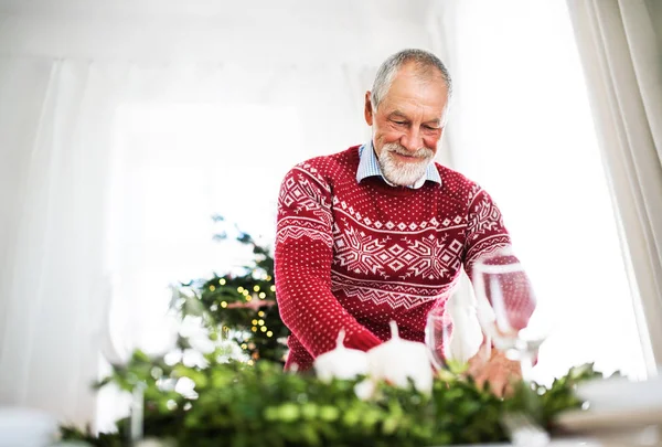 Un aîné met une table pour un dîner à la maison à Noël . — Photo