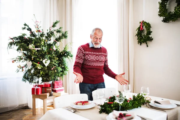 Um homem sênior em pé ao lado de uma mesa posta para um jantar em casa na época do Natal . — Fotografia de Stock