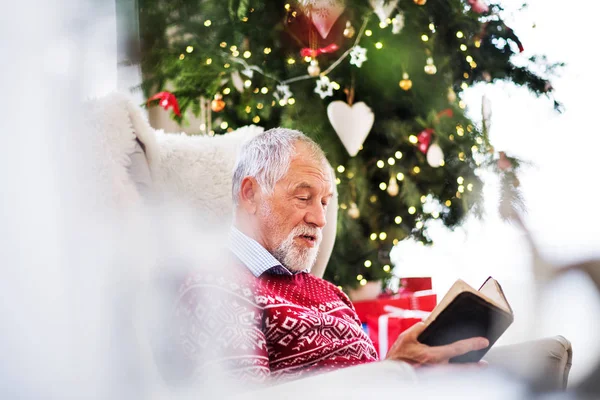 A senior man reading a book at home at Christmas time. — Stock Photo, Image