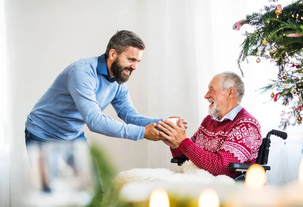 Un hipster donnant à boire à son père aîné en fauteuil roulant au temps de Noël . — Photo