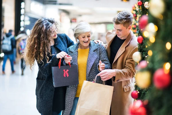 Een portret van een grootmoeder en tiener kleinkinderen in shopping center op Kerstmis. — Stockfoto