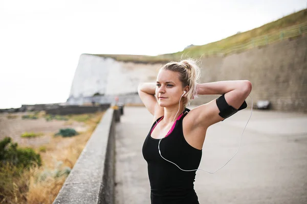 Giovane donna sportiva corridore con smartphone in piedi sulla spiaggia al di fuori . — Foto Stock