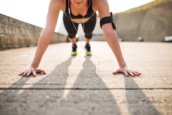 Giovane donna sportiva corridore con smartphone facendo flessioni al di fuori . — Foto Stock