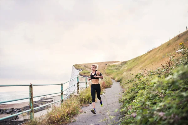 Young sporty woman runner with earphones running by sea in nature. — Stock Photo, Image