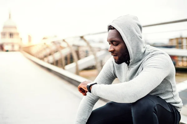Fiatal sportos fekete férfi futó intelligens nézni a hídon, egy város, pihenő. — Stock Fotó
