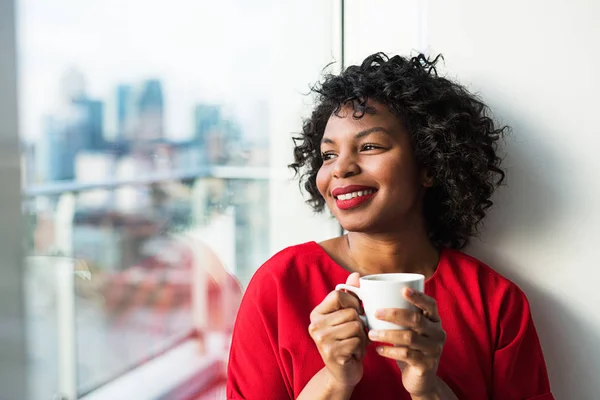 Kahve fincanı holding cam kenarında duran bir kadın bir close-up. — Stok fotoğraf