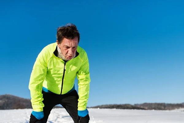 Een portret van senior man die na de run in de winter natuur. — Stockfoto