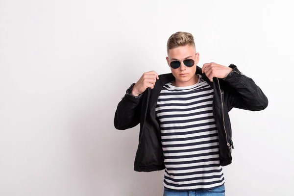 Ein selbstbewusster junger Mann mit Sonnenbrille in einem Studio, der ein gestreiftes T-Shirt trägt. — Stockfoto