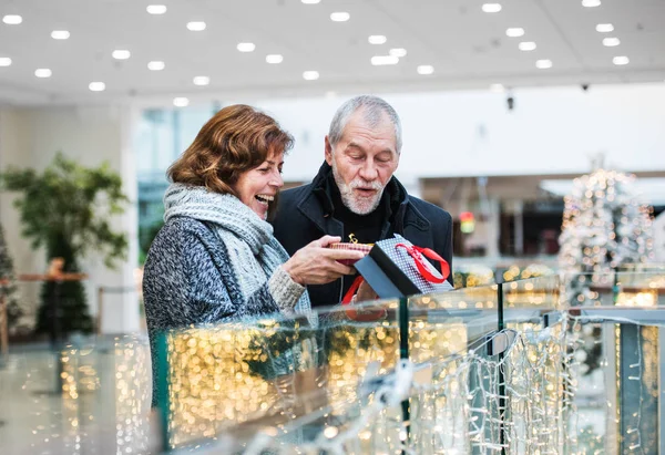 A senior woman giving a present to a man in shopping center at Christmas time. — Stock Photo, Image