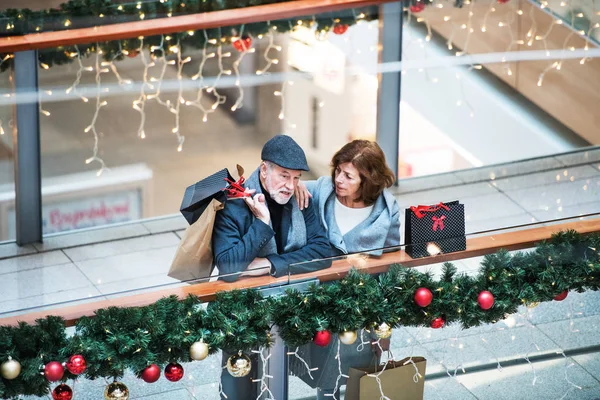 Een senior paar met papieren zakken in shopping center op Kerstmis. — Stockfoto