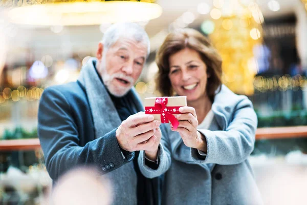 Ένα πορτρέτο του ανώτερος ζευγάρι με ένα δώρο στο εμπορικό κέντρο Χριστούγεννα. — Φωτογραφία Αρχείου