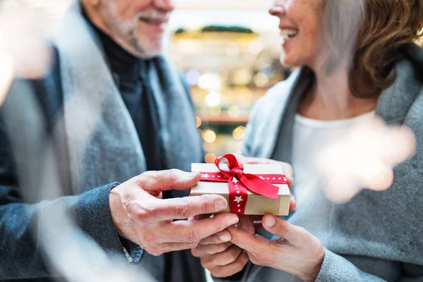 Una coppia anziana irriconoscibile con un regalo nel centro commerciale nel periodo natalizio . — Foto Stock