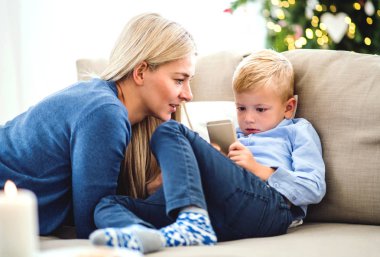 Bir anne ve küçük çocuk Noel zamanda evde kanepede oturan smartphone ile.