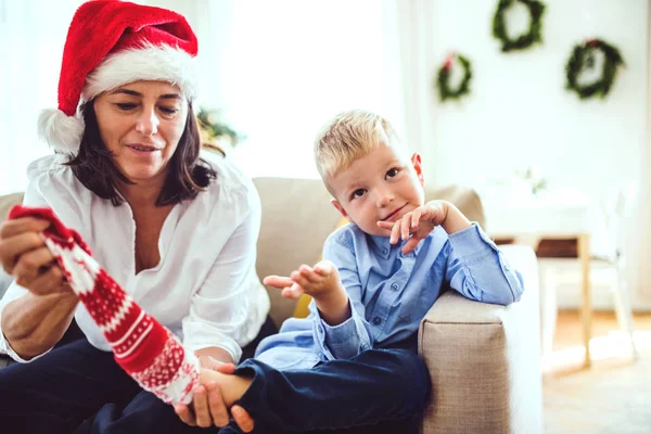 A small boy and grandmother with a Santa hat sitting on a sofa at home at Christmas time. — Stock Photo, Image