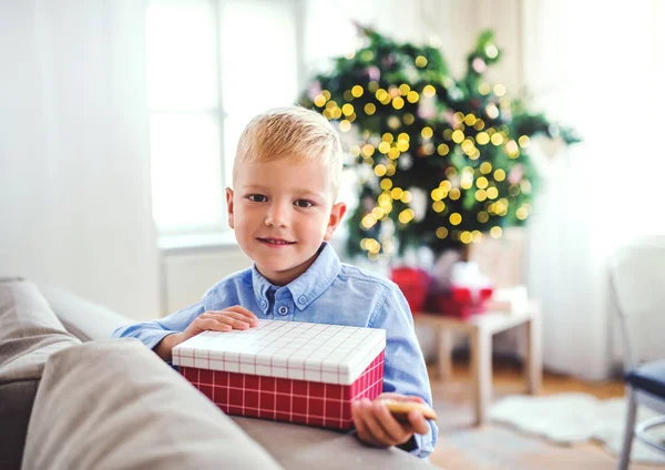 Um menino pequeno com um presente em casa na época do Natal . — Fotografia de Stock