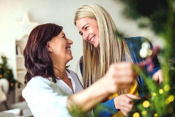 Seniorin mit erwachsener Tochter steht zu Hause am Weihnachtsbaum. — Stockfoto