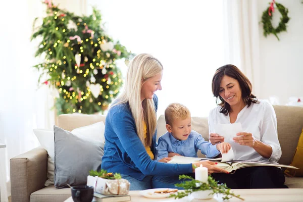 Ein kleiner Junge mit Mutter und Großmutter beim Betrachten von Fotos zu Hause zur Weihnachtszeit. — Stockfoto