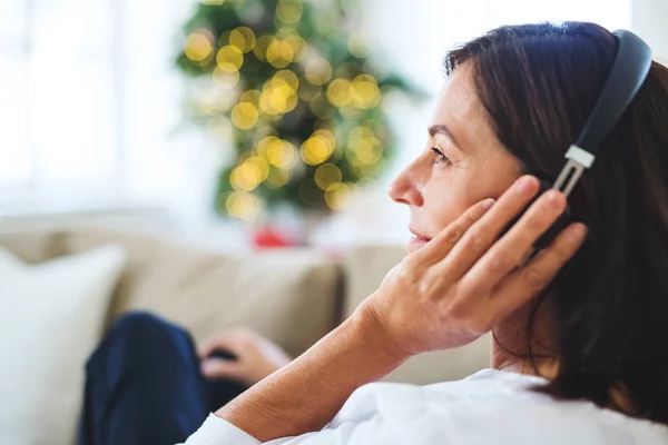 Uma mulher idosa com fones de ouvido ouvindo música em casa na época do Natal . — Fotografia de Stock