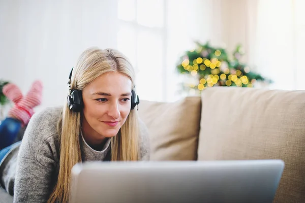 Uma jovem mulher com fones de ouvido e laptop em casa na época do Natal . — Fotografia de Stock