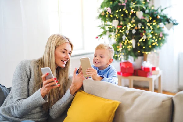 一个母亲和小男孩与智能手机坐在沙发上, 在圣诞节的时候. — 图库照片