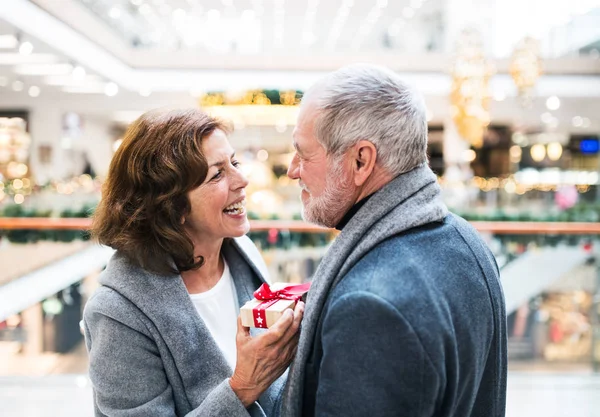 Ένας ανώτερος άνθρωπος δίνοντας ένα δώρο για μια γυναίκα στο εμπορικό κέντρο Χριστούγεννα. — Φωτογραφία Αρχείου