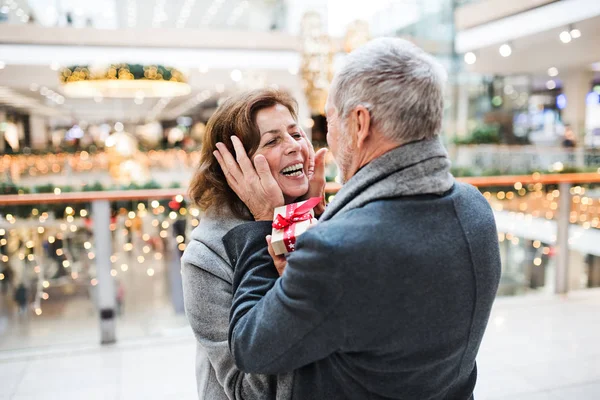 A senior man giving a present to a woman at shopping center at Christmas time. — Stock Photo, Image