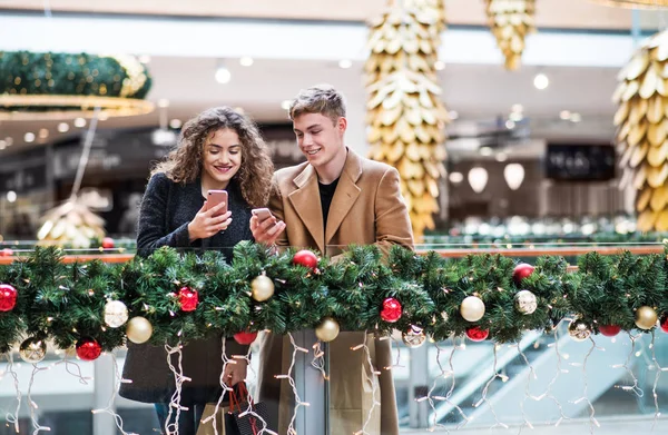 A young couple with smartphone in shopping center at Christmas. — Stock Photo, Image