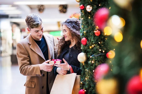 Een jonge man die een cadeautje geven aan zijn girfriend in winkelcentrum met Kerstmis. — Stockfoto