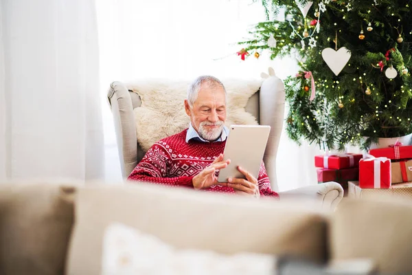 Портрет старшого чоловіка з планшетом, що сидить на кріслі вдома в різдвяний час . — стокове фото