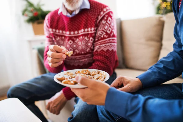 Pai sênior irreconhecível e filho adulto sentado em um sofá na época do Natal, comendo biscoitos . — Fotografia de Stock