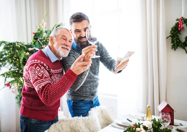 Um pai sênior e um filho adulto colocando uma mesa para o jantar na época do Natal . — Fotografia de Stock