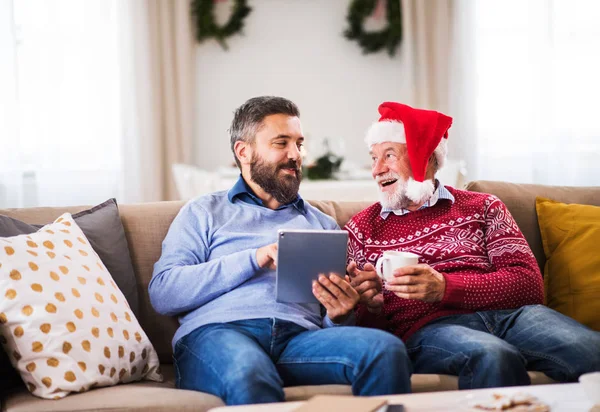 Bir üst düzey baba ve Noel zamanı evde kanepede oturan tablet ile yetişkin oğlu.