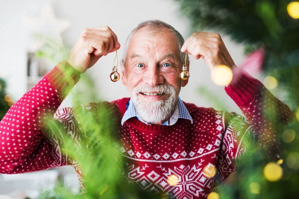 En ældre mand stående ved juletræ, holder bolde ornamenter . Stock-billede