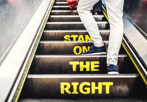 Piernas de un hombre usando escaleras mecánicas en la ciudad, viajando al trabajo. Vista trasera . — Foto de Stock