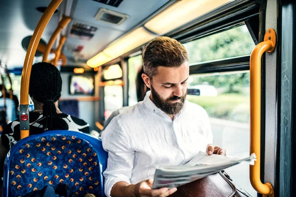 Hipster hombre en un autobús en la ciudad, viajando al trabajo y leyendo periódicos . — Foto de Stock