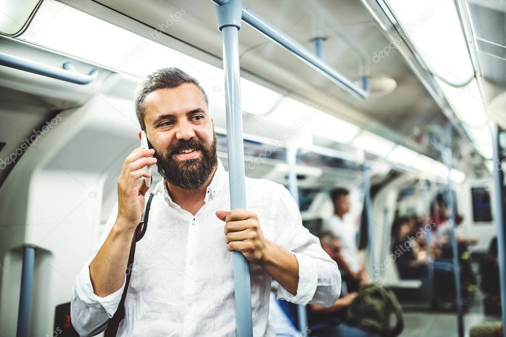 Hipster businessman with smartphone inside the subway in the city, travelling to work.